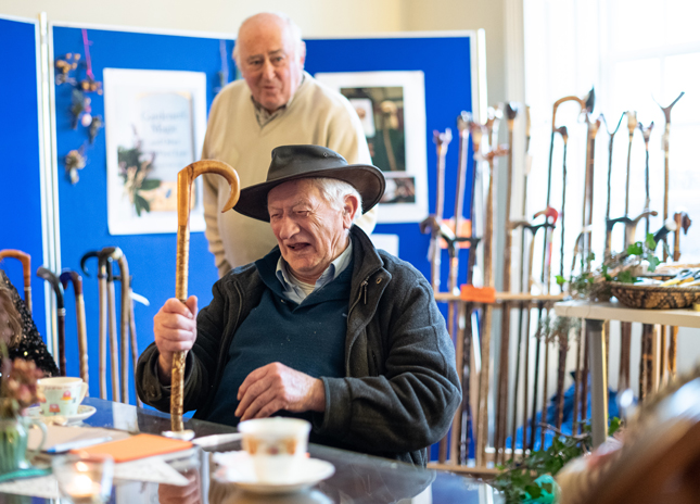 Two older men exchange stories inspired by walking sticks and the materials used in making them
