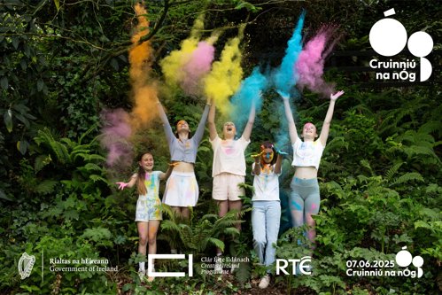 Five girls jump with arms in the air throwing colour powder above their heads.