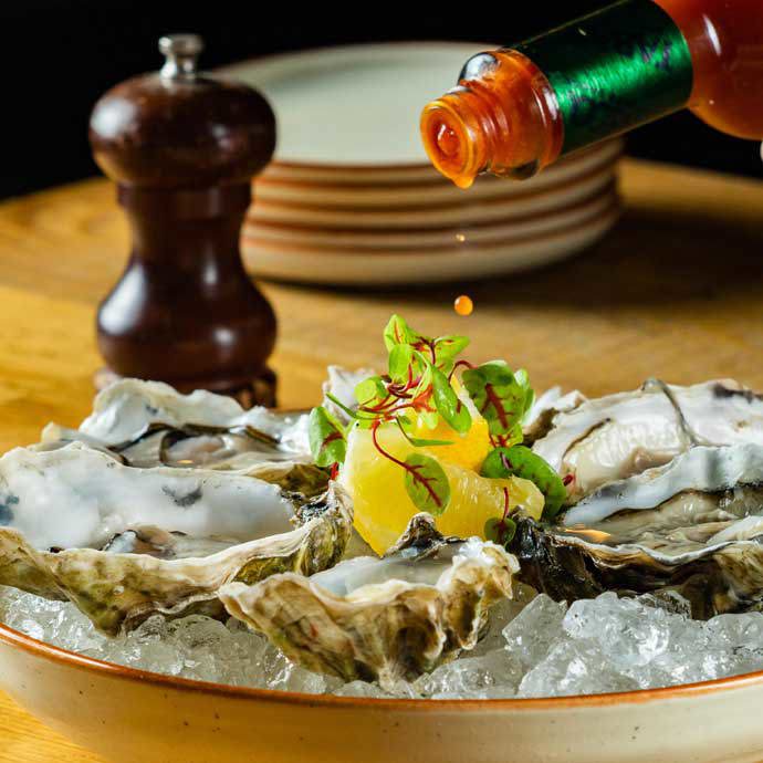 Plate of oysters with tobasco being poured on top