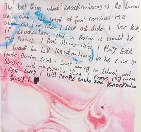 Child's marbled art work with a handwritten message saying "The best thing about Knocknaheeny  is the humour and club. The smell of food reminds me of my home. When I step out side I see kids. If Knocknaheeny was a person it would be my family. I feel strong when I play GAA. I want to tell Knocknaheeny to be nice to people. During Covid I loved having no school and staying with my parents. When I rome my area I feel happy. I wish people could see Knocknaheeny. - Lucy C"