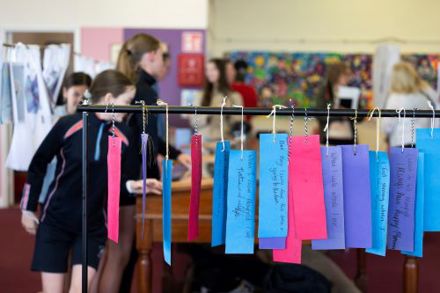 Blue, pink and purple paper tags hang from a rail in Mayfield Library, each inscribed with a handwritten message. Children are in the background.