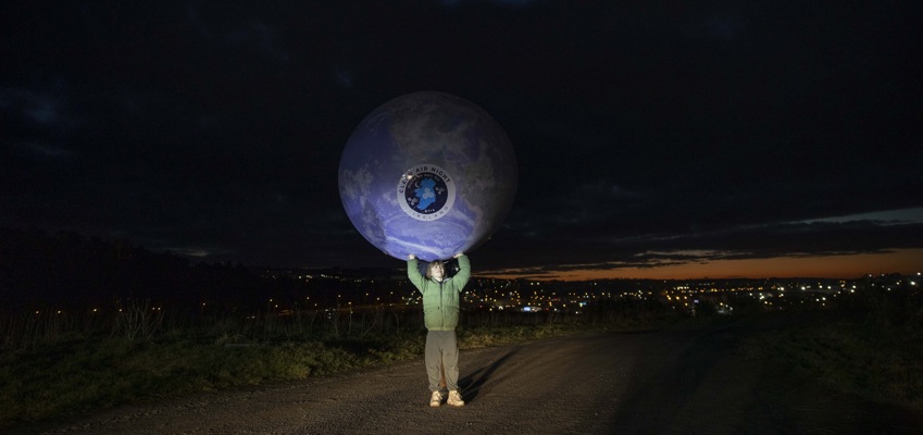 A young person holding a replica of the earth overhead