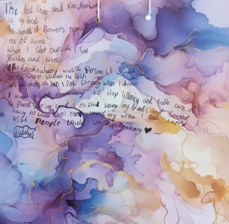 Child's marbled painting with handwritten message: "The best thing about Knocknaheeny is the food. The smell of flowers reminds me of home. When I step outside I see bushes and trees. If Knocknaheeny was a person it would be my sister because the feilds are as pretty as her. I feel strong when I dance. I want to tell Knocknaheeny to stop littering and take care of the planet. During Covid I missed seeing my friends and loved having no school. When I roam around my area I feel happy. I wish people could see Knocknaheeny. - Natalia"