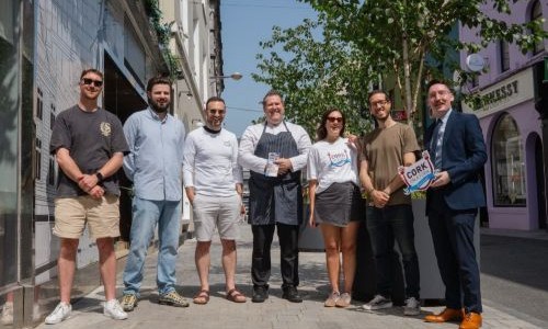 Business people from Pembroke Street lined up on the street with blue skies holding Cork on a Fork festival signage