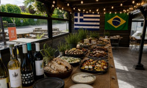 Table of food on display with Greek and Brazilian flags behind