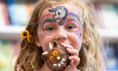 Girl with face-paint holding chocolate cupcake