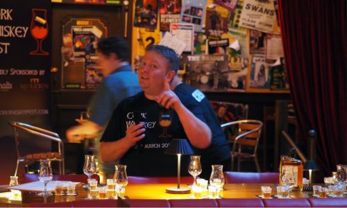 A person holding a whiskey bottle at a table in a bar