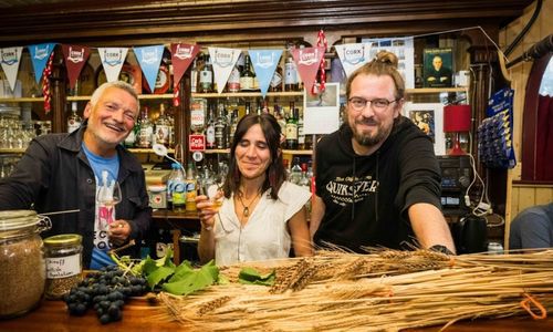 Three people behind the bar at the sourdough and wine harvest bread making and natural wine event wheat on the bar