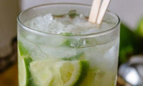 Glass of ice with lime and clear drink with two stirrers