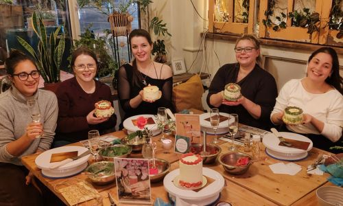 Five ladies sitting around a wooden table with glasses of prosecco showing off the cakes they decorated