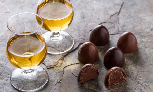 two glasses of whiskey beside pieces of chocolate