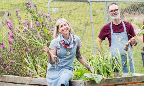 Two owners of Co Op in their garden with fresh produce from the garden