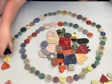 Spiral of small painted mosaic tiles, circular and heart shaped, surrounding a central arrangement of more tiles in various shapes and colours