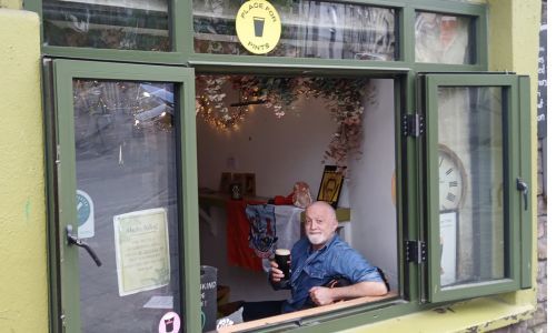 A man holds up a pint glass of stout looking out the window of a pub